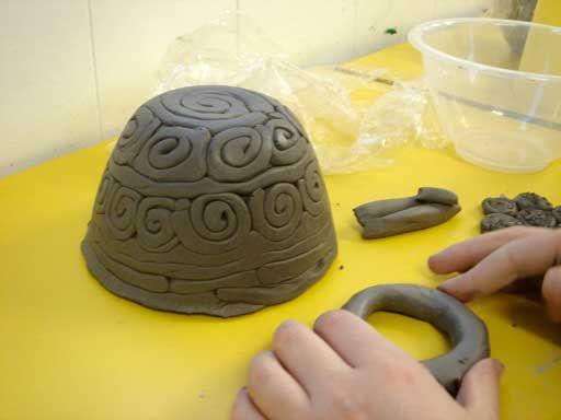 Pictured: Child's hand pressing on clay in front of small bowl with textured swirls