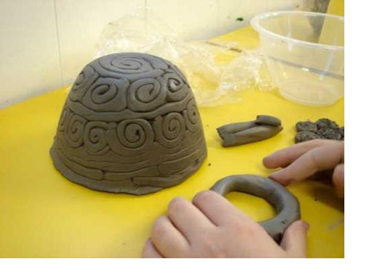 Pictured: Child's hand pressing on clay in front of small bowl with textured swirls